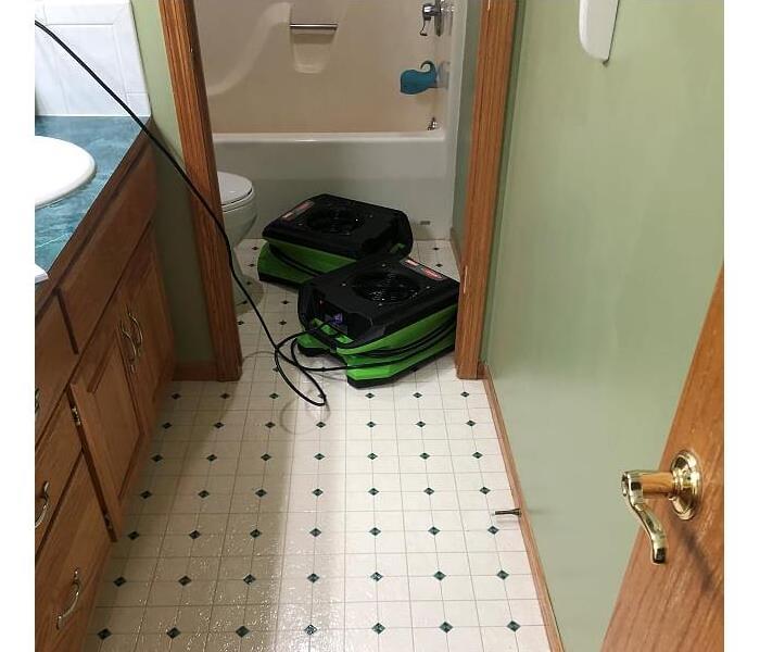 bathroom with green diamond and white flooring and two air green and black SERVPRO air movers plugged in