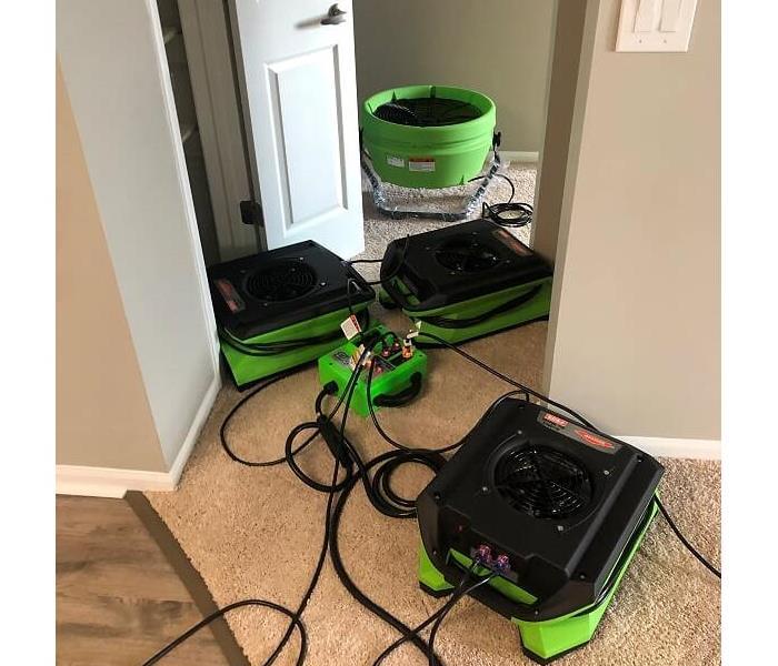 several green and black air movers and one fan on tan carpet in a hallway 