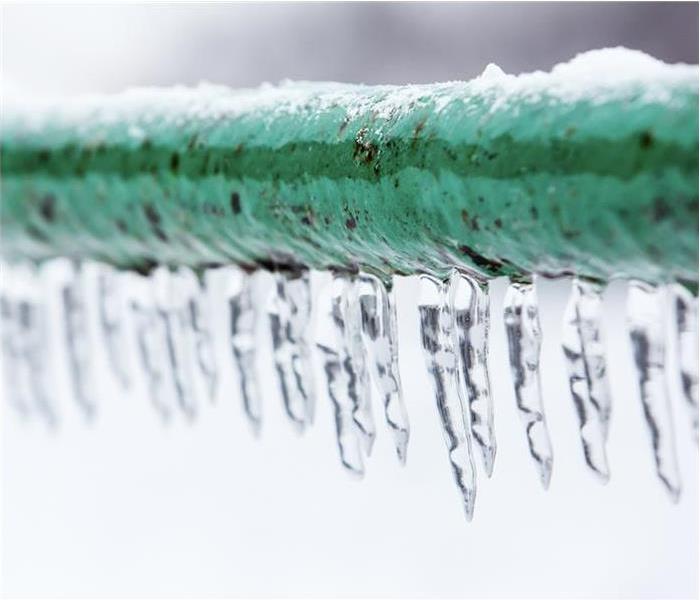 A green pipe that is frozen with icicles around it.