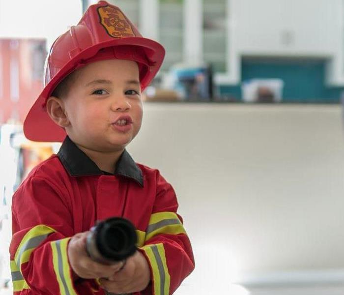 A little child holding a fire hose, wearing a fire hat.