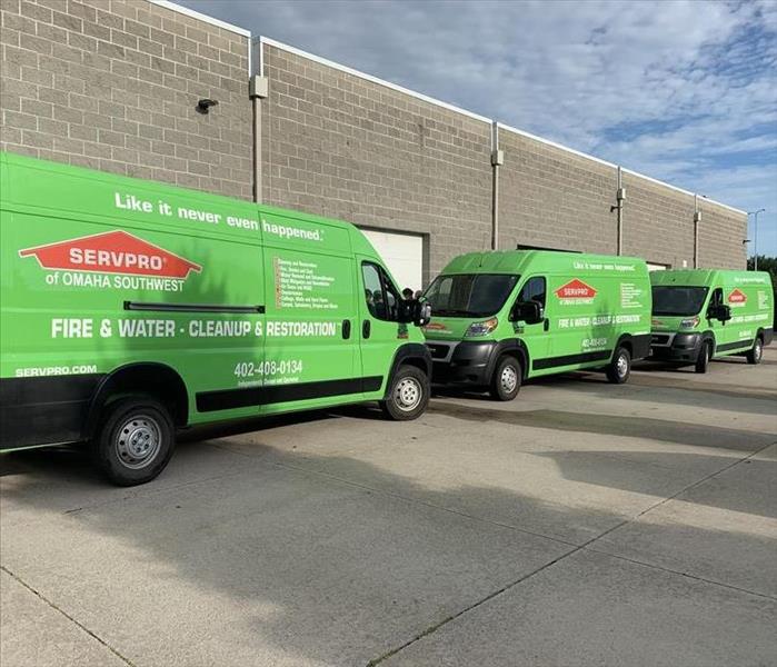 Three lime green vans with SERVPRO on the side, parked in front of a grey building.